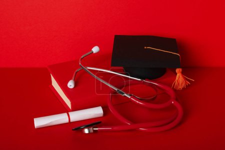 Téléchargez les photos : Chapeau diplômé avec diplôme et stéthoscope, sur fond rouge. - en image libre de droit