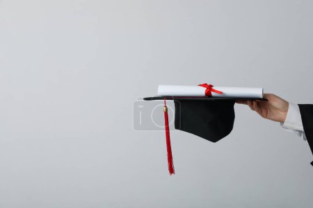 Téléchargez les photos : Diplôme et chapeau d'un diplômé universitaire, sur fond gris. - en image libre de droit