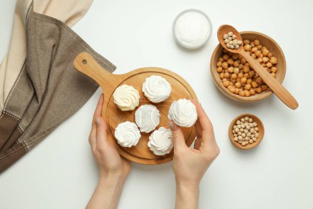 Marshmallows on board in hands, towel and bowls with chickpeas and cream on white background, top view