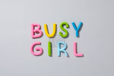 La palabra "chica ocupada" de plastilina de color sobre un fondo gris.