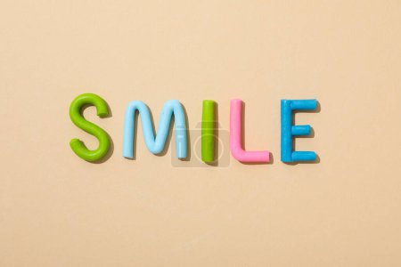 Das Wort: "Lächeln" aus farbigem Knetmasse auf einem Pfirsichhintergrund.