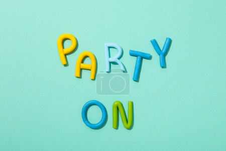 La palabra "fiesta" está hecha de plastilina de color sobre un fondo turquesa.