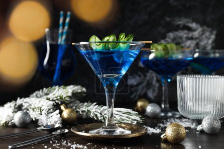 Blauer Cocktail in Gläsern, Weihnachtsbaumzweige mit Schnee und Kugeln auf Holzgrund, Nahaufnahme