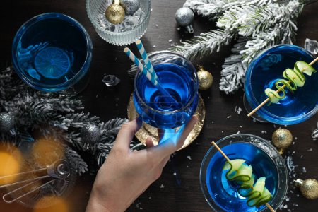Foto de Cóctel azul en vasos, mano, ramas de árbol de Navidad con nieve y bolas sobre fondo de madera, vista superior - Imagen libre de derechos