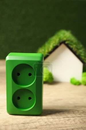 Toma eléctrica verde con casa decorativa sobre fondo