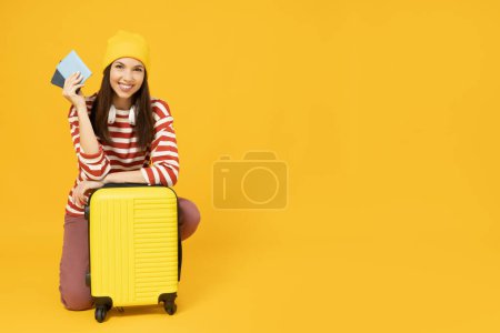 Young girl with suitcase and passport on yellow background, space for text