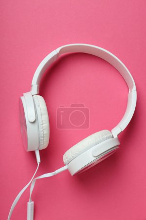 White, on-ear headphones with a wire on a pink background.