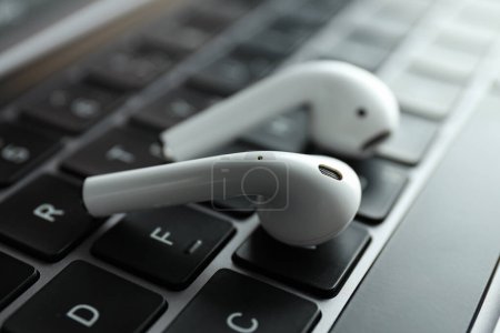 White, headphones, in-ears on the laptop keyboard.