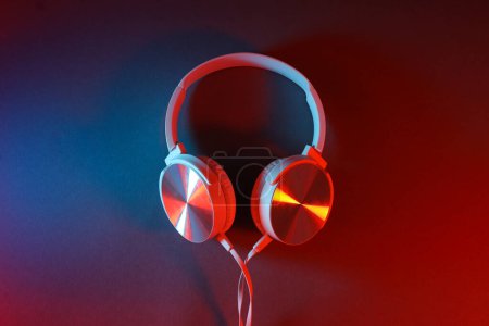 White, over-the-ear headphones with a wire on a colored, dark background.