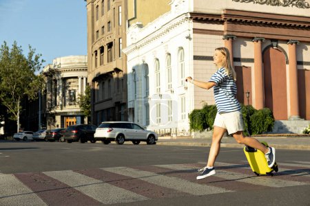 Ein Mädchen, blond, mit einem gelben Koffer auf der Straße.