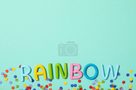 La palabra "arco iris" está hecha de plastilina de color sobre un fondo turquesa.
