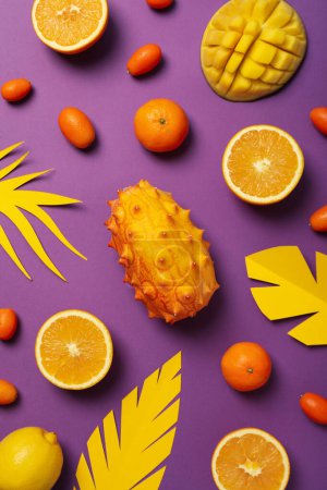 Tropical fruit and paper leaves on purple background, top view