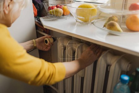 Téléchargez les photos : Femme ajustant la température d'un radiateur à la maison - en image libre de droit