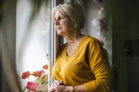 Photo for Worried elderly woman looking in window - Royalty Free Image