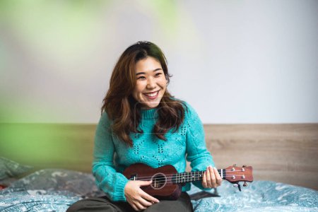 Photo for Young woman having fun playing Ukulele in her studio apartment - Royalty Free Image