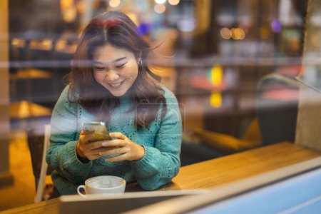 Téléchargez les photos : Jeune femme utilisant un téléphone portable dans un café - en image libre de droit