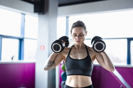 Photo for Young woman exercising with dumbbells in a health club - Royalty Free Image