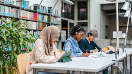 Foto de Grupo multiétnico de estudiantes sentados en una biblioteca y estudiando juntos - Imagen libre de derechos