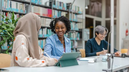Téléchargez les photos : Groupe multiethnique d'étudiants assis dans une bibliothèque et étudiant ensemble - en image libre de droit