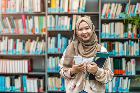 Téléchargez les photos : Portrait d'une étudiante musulmane asiatique debout dans une bibliothèque - en image libre de droit