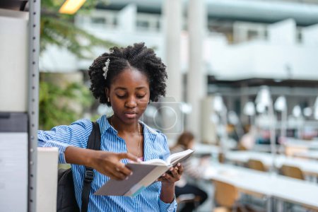Téléchargez les photos : Femme noire étudiant lisant un livre dans une bibliothèque - en image libre de droit