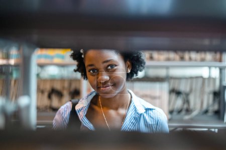 Téléchargez les photos : Portrait d'une étudiante noire debout dans une bibliothèque - en image libre de droit