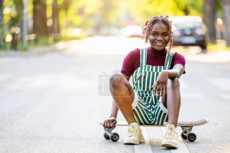 Photo for Portrait of a black non-binary person with a skateboard sitting on the street - Royalty Free Image