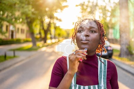 Photo for Black non-binary person smoking electronic cigarette in the street - Royalty Free Image