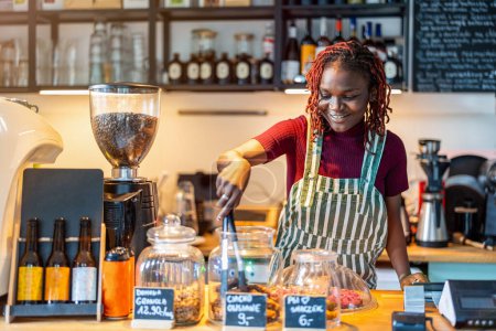 Photo for Portrait of a genderqueer barista making coffee at counter in coffee shopThe meaning of the inscriptions on the counter: "homemade granola", "oatmeal cookie", "dog treat". - Royalty Free Image
