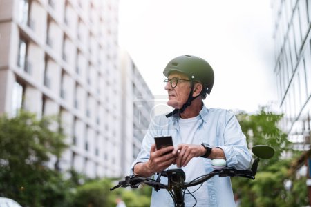 Photo for Mature man using mobile phone while riding bicycle in the city - Royalty Free Image