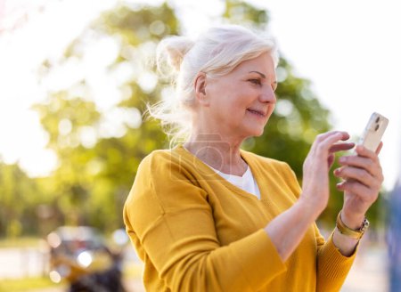 Photo for Senior woman using smartphone outdoors - Royalty Free Image