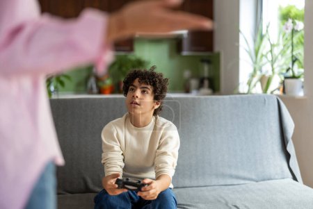 Téléchargez les photos : Adolescent garçon jouer à des jeux vidéo alors que sa mère n'est pas heureux à ce sujet - en image libre de droit