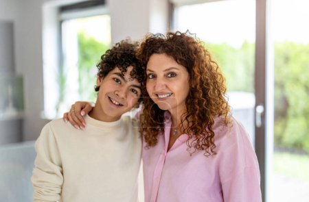 Téléchargez les photos : Portrait de mère et fils souriants debout dans le salon à la maison - en image libre de droit