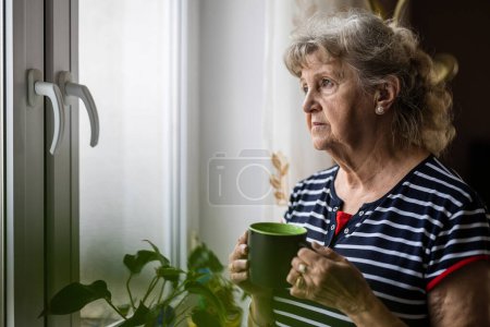 Téléchargez les photos : Portrait de femme âgée regardant par la fenêtre - en image libre de droit