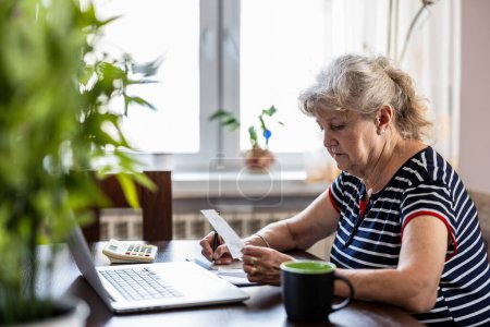 Téléchargez les photos : Femme âgée passant en revue ses finances à la maison - en image libre de droit