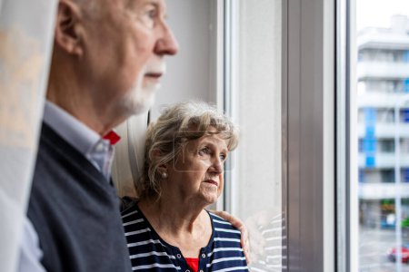 Téléchargez les photos : Portrait de couple de personnes âgées regardant par la fenêtre à la maison - en image libre de droit