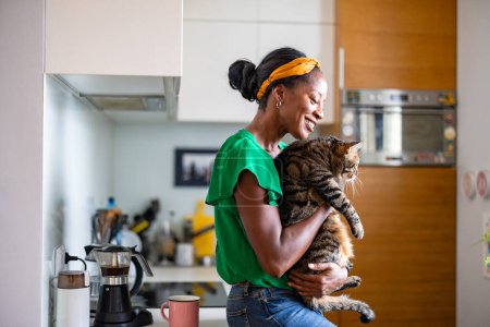 Foto de Mujer sonriente sosteniendo a su gato en casa - Imagen libre de derechos