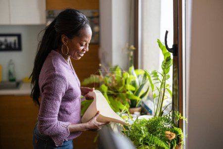 Téléchargez les photos : Belle femme arrosant des plantes à la maison - en image libre de droit