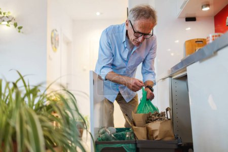 Foto de Hombre mayor clasificando basura en papeleras de reciclaje en casa - Imagen libre de derechos