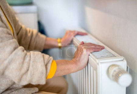 Téléchargez les photos : Femme âgée vérifiant radiateur de chauffage dans son appartement - en image libre de droit