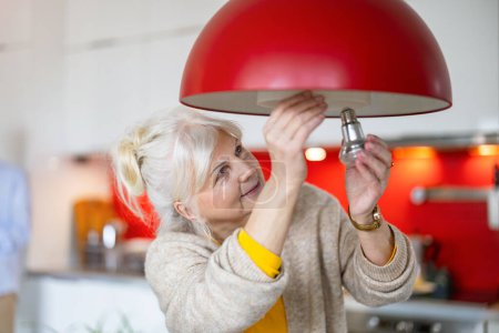 Photo for Senior woman changing light bulb in her home - Royalty Free Image