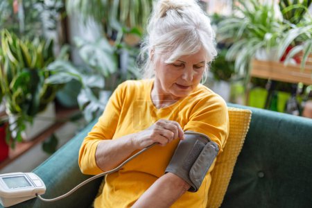Foto de Mujer mayor midiendo su presión arterial mientras está sentada en un sofá en casa - Imagen libre de derechos