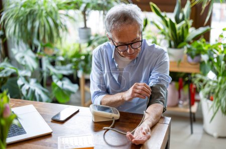 Téléchargez les photos : Homme âgé mesurant la pression artérielle à la maison - en image libre de droit