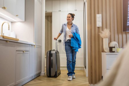 Téléchargez les photos : Jeune femme entrant appartement loué avec bagages - en image libre de droit