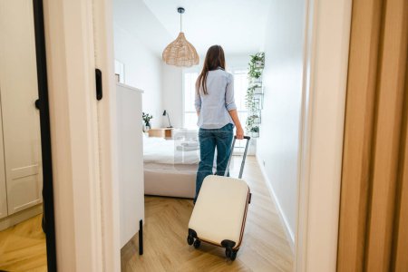 Vista trasera de una joven que entra en una habitación de hotel con su equipaje