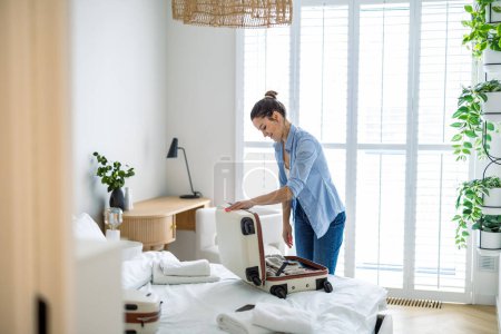 Young woman packing suitcase in the bedroom, preparing for travel
