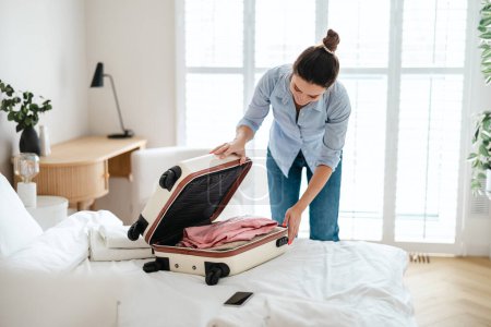 Foto de Joven mujer haciendo las maletas en el dormitorio, preparándose para viajar - Imagen libre de derechos