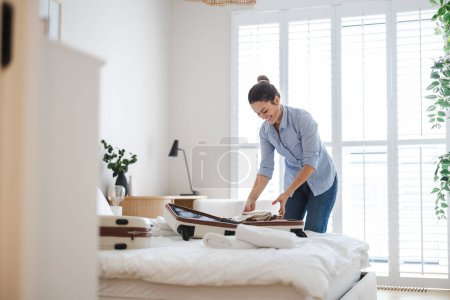 Foto de Joven mujer haciendo las maletas en el dormitorio, preparándose para viajar - Imagen libre de derechos