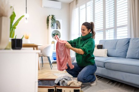 Téléchargez les photos : Jeune femme déballer ses vêtements dans un appartement loué - en image libre de droit
