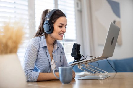 Photo for Woman wearing headphones sitting at a desk speaking into microphone and recording a podcast - Royalty Free Image